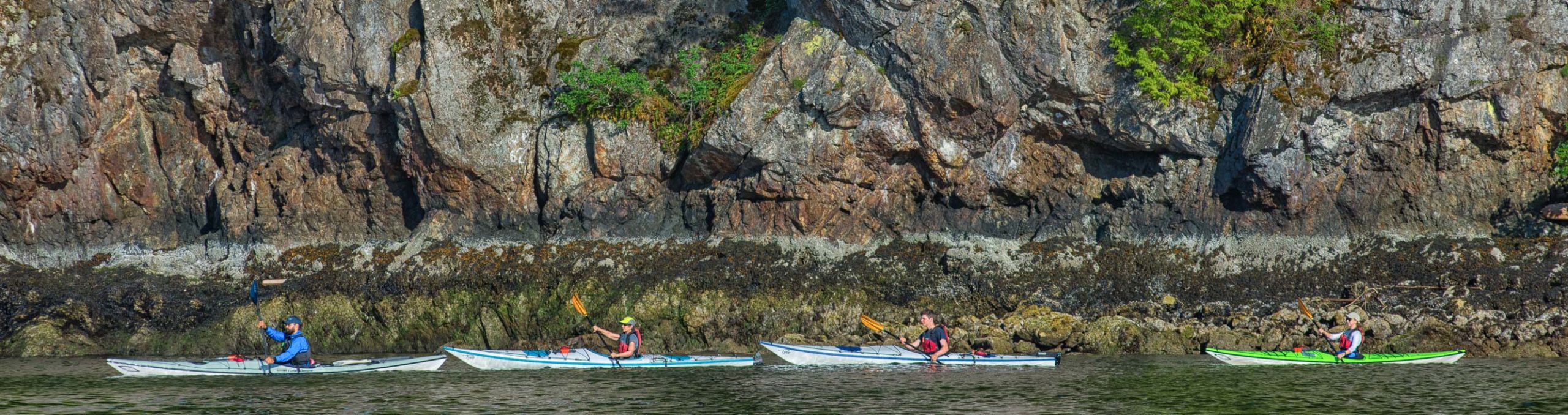 Group of kayakers along a rock face