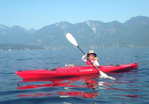 Child kayaking in a red kayak with mountains in the backgroun