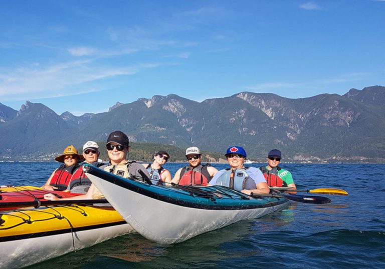 Men and women kayaking with mountains in the background
